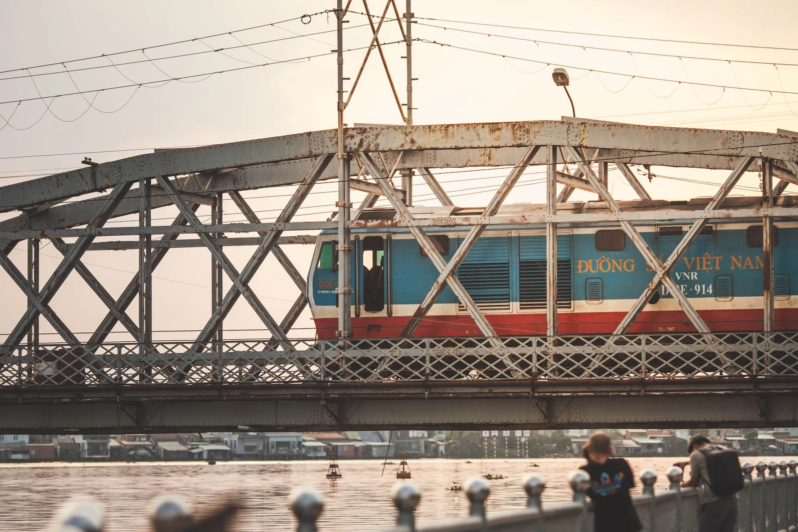 Локомотив Vietnam Railways с надписью Duong Sat Viet Nam пересекает мост на закате