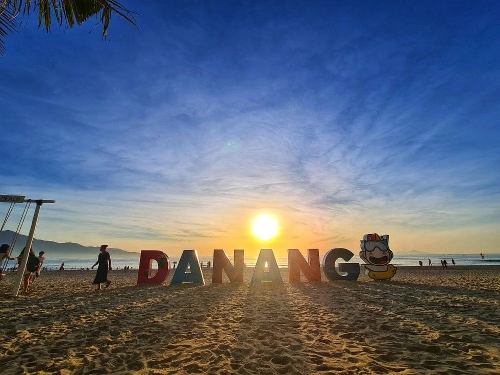 Вывеска DANANG на пляже на закате, люди рядом